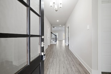 This photo shows a bright, welcoming entryway with a modern chandelier, light wood flooring, and a view into a spacious, open-plan living area. The open door reveals a sleek design with neutral walls and recessed lighting, offering a stylish and inviting first impression.