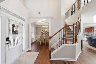 Entrance foyer with a towering ceiling, dark wood-type flooring, a chandelier, crown molding, and stairway
