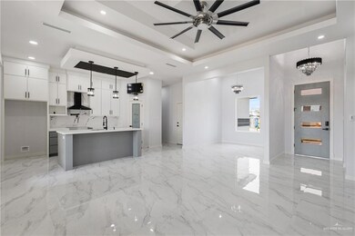 Kitchen featuring white cabinetry, hanging light fixtures, wall chimney range hood, and a raised ceiling