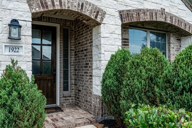 The sidewalk leads up to a majestic stone and brick exterior, surrounded by landscaping creating beautiful curb appeal.