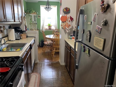 Kitchen with stainless steel appliances, light countertops, dark brown cabinetry, hanging light fixtures, and crown molding