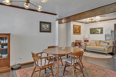 Dining room featuring dark wood-style flooring, baseboards, crown molding, a textured wall, and a chandelier