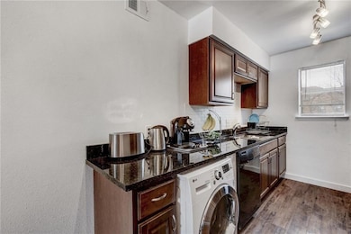 Kitchen featuring washer / clothes dryer, wood finished floors, black dishwasher, dark stone counters, and tasteful backsplash
