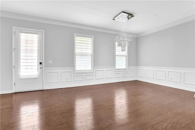 Unfurnished dining area with a chandelier, healthy amount of natural light, ornamental molding, wainscoting, and dark wood finished floors