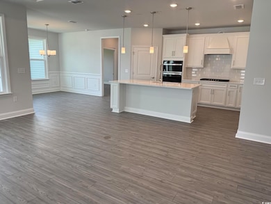 Kitchen with double oven, gas stovetop, custom range hood, light countertops, and dark wood finished floors