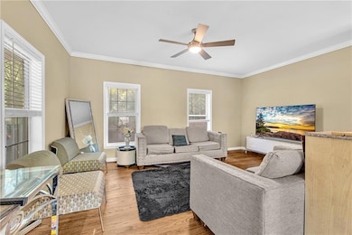 Living area with plenty of natural light, a ceiling fan, ornamental molding, wood finished floors, and baseboards