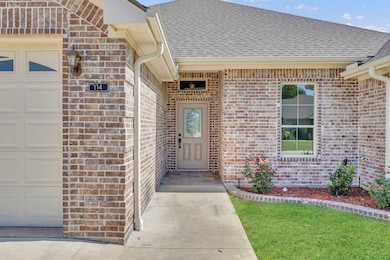 View of exterior entry featuring a shingled roof, brick siding, and an attached garage