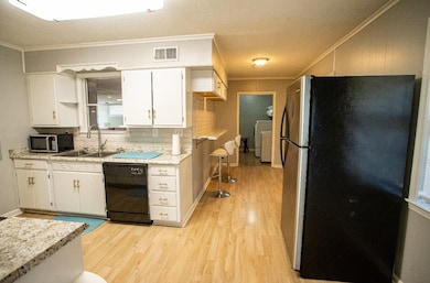 Kitchen with stainless steel appliances, ornamental molding, light wood-type flooring, a sink, and white cabinetry