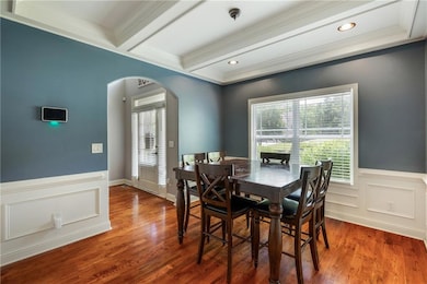 Dining room featuring arched walkways, ornamental molding, beam ceiling, a wainscoted wall, and wood finished floors