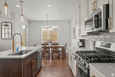 Kitchen featuring stainless steel appliances, hanging light fixtures, light stone counters, dark wood-style flooring, and recessed lighting