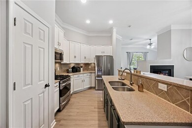 Kitchen featuring appliances with stainless steel finishes, a kitchen island with sink, crown molding, ceiling fan, and a glass covered fireplace