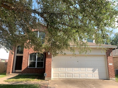View of property hidden behind natural elements with concrete driveway and brick siding