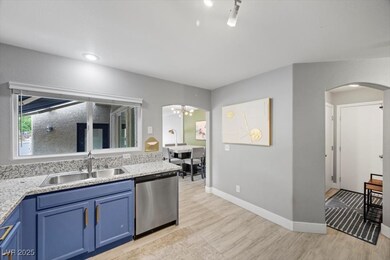 Kitchen with blue cabinets, arched walkways, stainless steel dishwasher, a chandelier, and light stone countertops